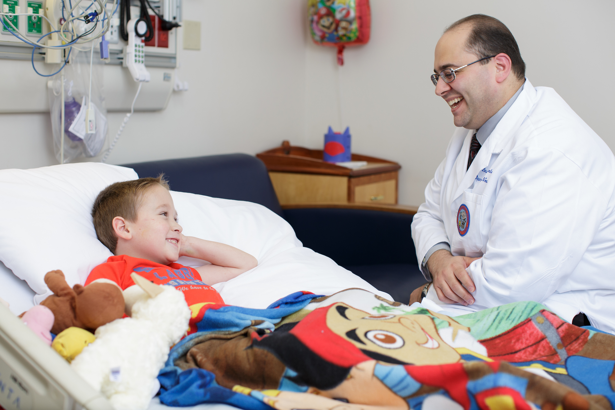 UF Health Children's Hospital neurosurgeon laughs with a young male patient who is lying down in a hospital bed.