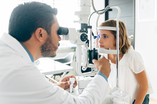 A male ophthalmologist uses a magnifying device to peer into a young female patients eyes.