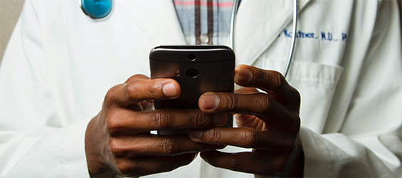 A male African-American doctor types on his smartphone.