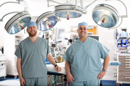 Two pediatric neurosurgeons stand proudly in an operating room environment