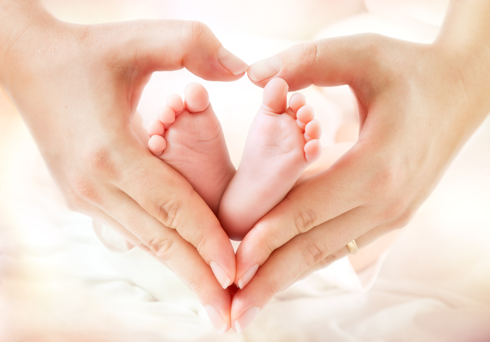 two hands making a heart shape around two baby feet