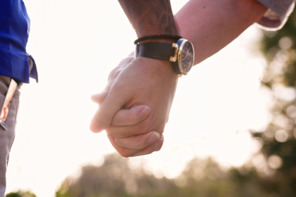 A closely cropped image of a man and woman holding hands in a sunlit field.