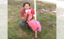 A woman crouching down on the ground posing with a flamingo figurine wearing a santa hat